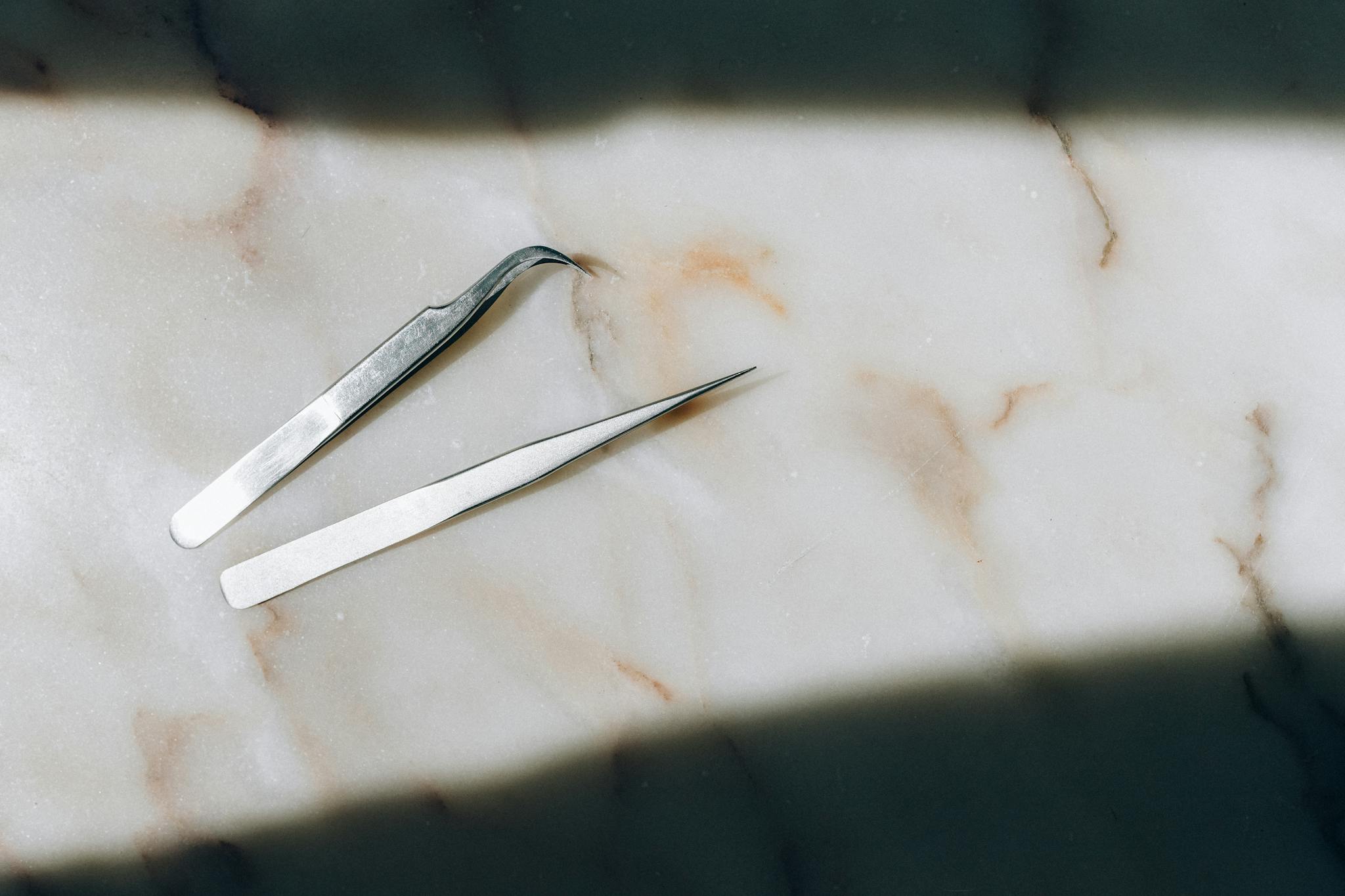 High-angle shot of two precision tweezers on a marble surface, highlighting elegance and simplicity.
